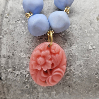 Necklace with blue beads and a pink floral pendant on a textured surface