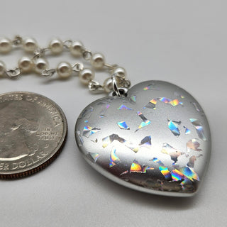 Heart-shaped silver pendant with colorful inclusions next to a quarter on a gray background