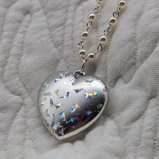 Heart-shaped silver pendant with colorful accents on a white fabric background