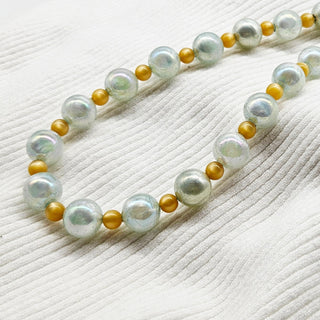 Pearlized and golden bead necklace on a textured white surface