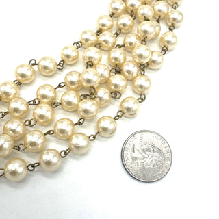 Pearl necklace with brass chain next to a U.S. quarter on a white background