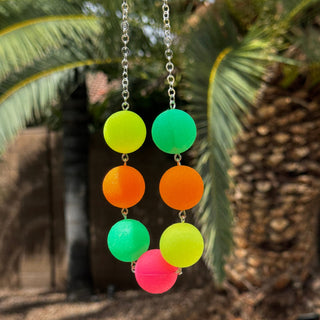 Neon-colored spherical beads on a chain against a palm tree background