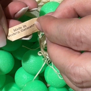 Hand holding a 'Made in Western Germany' tag over green beads