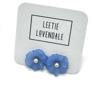Blue flower-shaped earrings with pearl centers on a Leetie Lovendale branded stand.