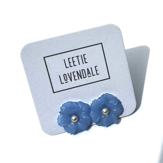 Blue flower-shaped earrings on a Leetie Lovendale branded card.