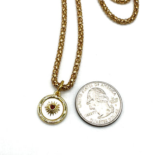 Gold necklace with a heart pendant next to a quarter on a white background