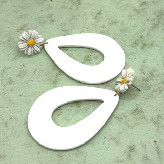 White teardrop-shaped earrings with floral details on a textured green surface