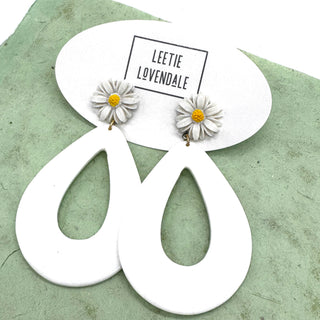 White earrings with floral designs on a green surface, featuring the brand 'LEETIE LOVENDALE'.