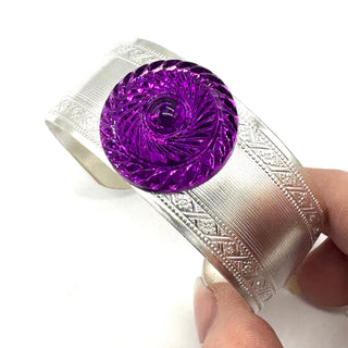 Silver bracelet with a purple lucite stone held by a hand on a white background