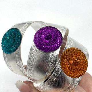 Silver bracelets with colorful circular stones held by a hand on a white background