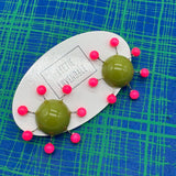 OlIve green earrings with hot pink beads radiating from center with posts on a blue and green plaid background.