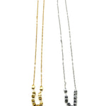 A pair of necklaces, in silver and gold, on a white background. Each is a fine chain with several cube beads at the center.