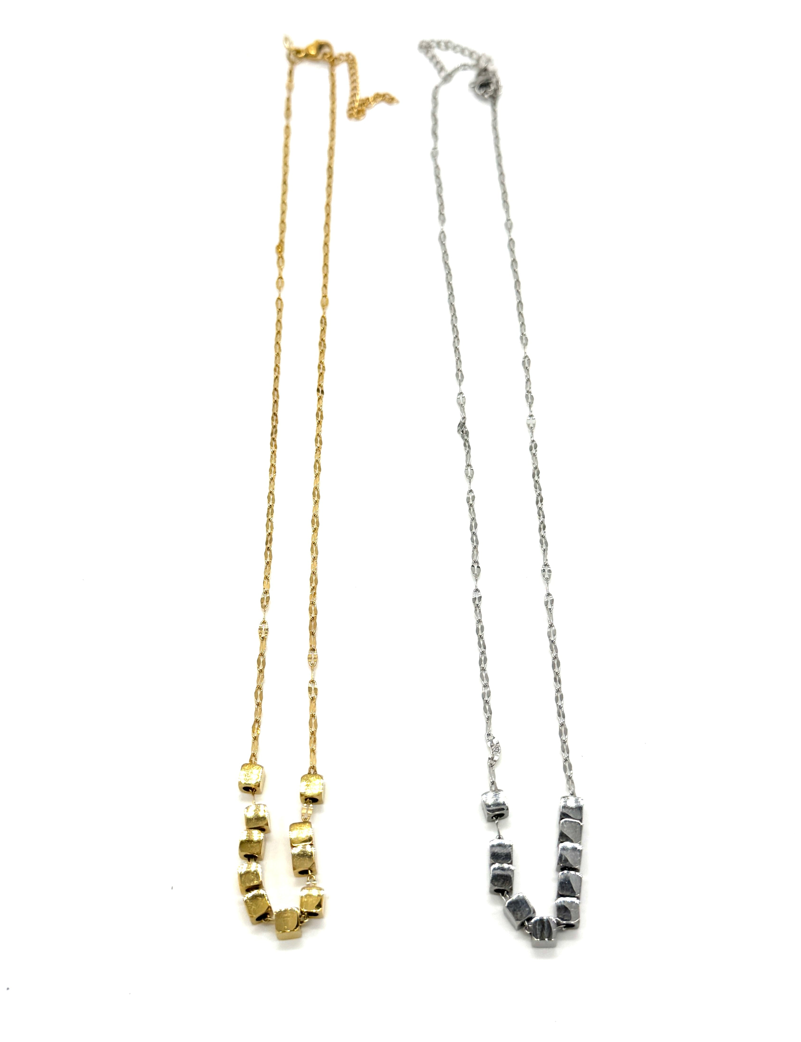 A pair of necklaces, in silver and gold, on a white background. Each is a fine chain with several cube beads at the center.