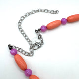 Close up of bright coral and pink beaded necklace's adjustable clasp on a white background.