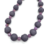 Closeup of necklace featuring dark gray and lilac lucite beads laid on a white background.