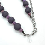 Closeup of adjustable necklace featuring dark gray and lilac lucite beads laid on a white background.
