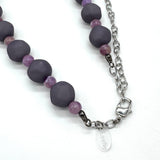 Closeup of adjustable necklace featuring dark gray and lilac lucite beads laid on a white background.
