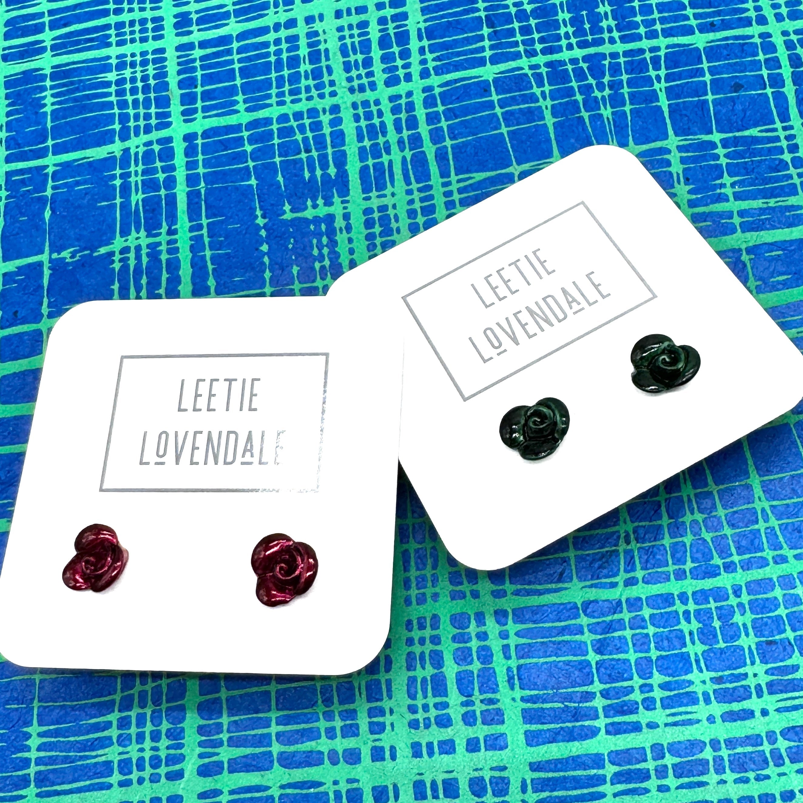 Two pairs of earrings on 'Leetie Lovendale' branded cards against a blue and green patterned background.