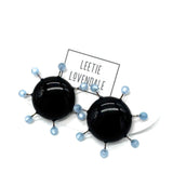 Black circular earrings with blue beads on a white background, featuring the brand 'Leetie Lovendale'.