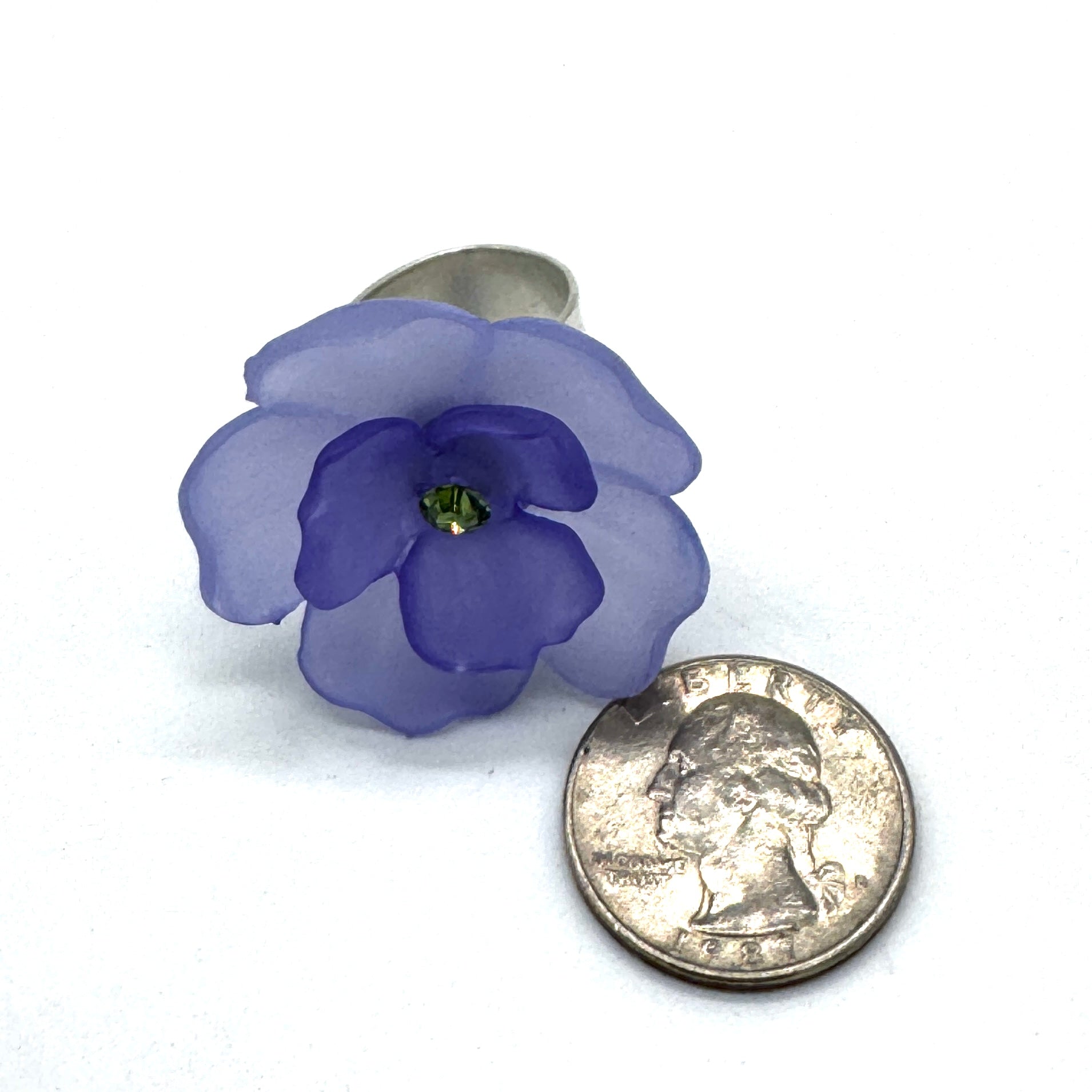 Teal and purple floral cocktail ring on a white background with a quarter for scale.