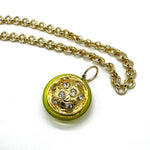 A gold chain necklace with a round pendant featuring a bright yellow-green border and a gold-toned center set with clear rhinestones, shown on a plain white background.