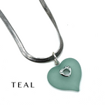 A teal heart-shaped pendant necklace with a silver snake chain and a small silver heart detail, shown on a white background with the word 'TEAL' printed in the lower left.