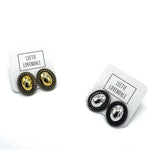 Two pairs of oval stud earrings on white display cards. One pair features gold metal with a textured border, and the other pair features silver metal with a textured border.