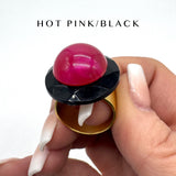 Hand holding a lip balm with a pink cap and black top, labeled 'HOT PINK/BLACK'.
