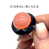 Hand holding a coral and black ring on a white background