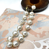 A strand of irregular white resin pearls with textured, hammered finishes, connected by gold-tone chains and clasps, displayed on a patterned beige and silver surface.
