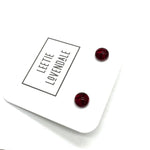A pair of small round stud earrings in deep red resin, displayed on a white branded card that reads 'LEETIE LOVENDALE'.