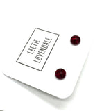 A pair of small round stud earrings in deep red resin, displayed on a white branded card that reads 'LEETIE LOVENDALE'.
