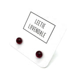 A pair of small round dark red stud earrings displayed on a white backing card with the brand name 'LEETIE LOVENDALE' printed in black text.