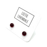 A pair of small round dark red stud earrings displayed on a white backing card with the brand name 'LEETIE LOVENDALE' printed in black text.