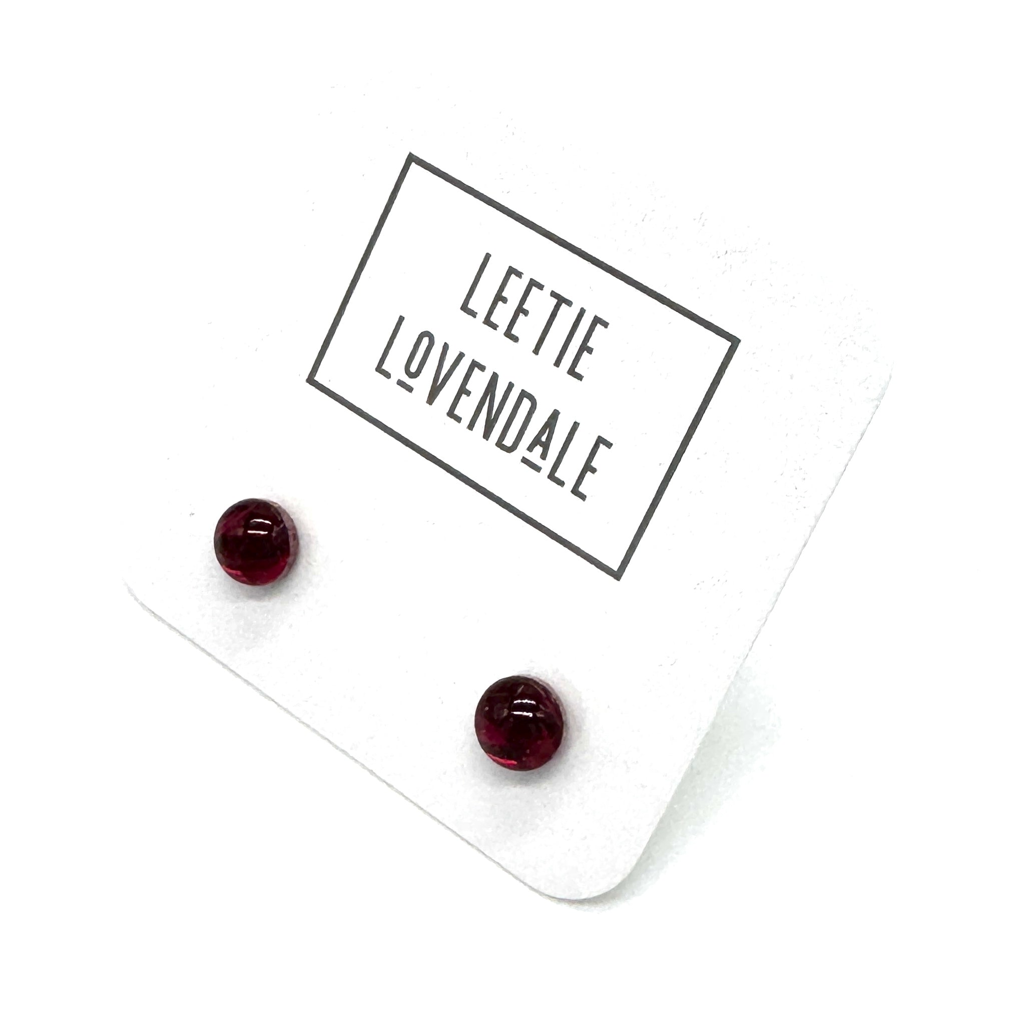 A pair of small round dark red stud earrings displayed on a white backing card with the brand name 'LEETIE LOVENDALE' printed in black text.