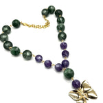 A beaded necklace featuring dark green and purple lucite beads connected by small gold links, with a gold butterfly pendant and gold chain clasp, shown on a plain white background.