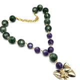 A beaded necklace featuring dark green and purple lucite beads connected by small gold links, with a gold butterfly pendant and gold chain clasp, shown on a plain white background.