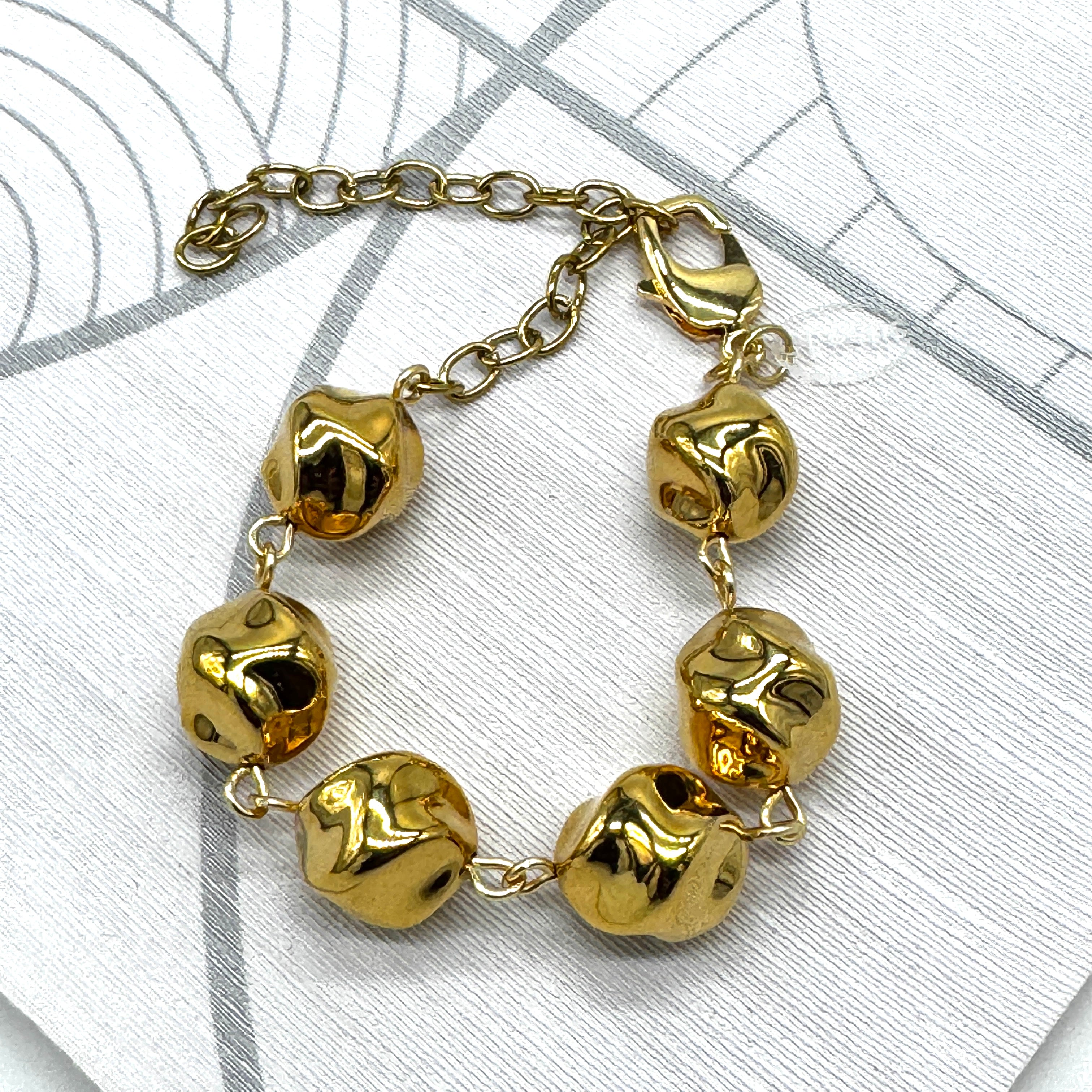 A gold-tone chain bracelet with six irregular, textured bead-like links, displayed on a light gray patterned surface.