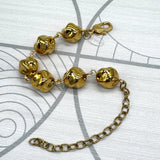 A gold-toned bracelet featuring textured, rounded beads connected by a delicate chain, with an adjustable lobster clasp and extender chain, displayed on a light gray patterned surface.