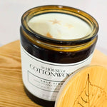 Candle in a glass jar labeled 'House of Cottonwood' on a bamboo surface.