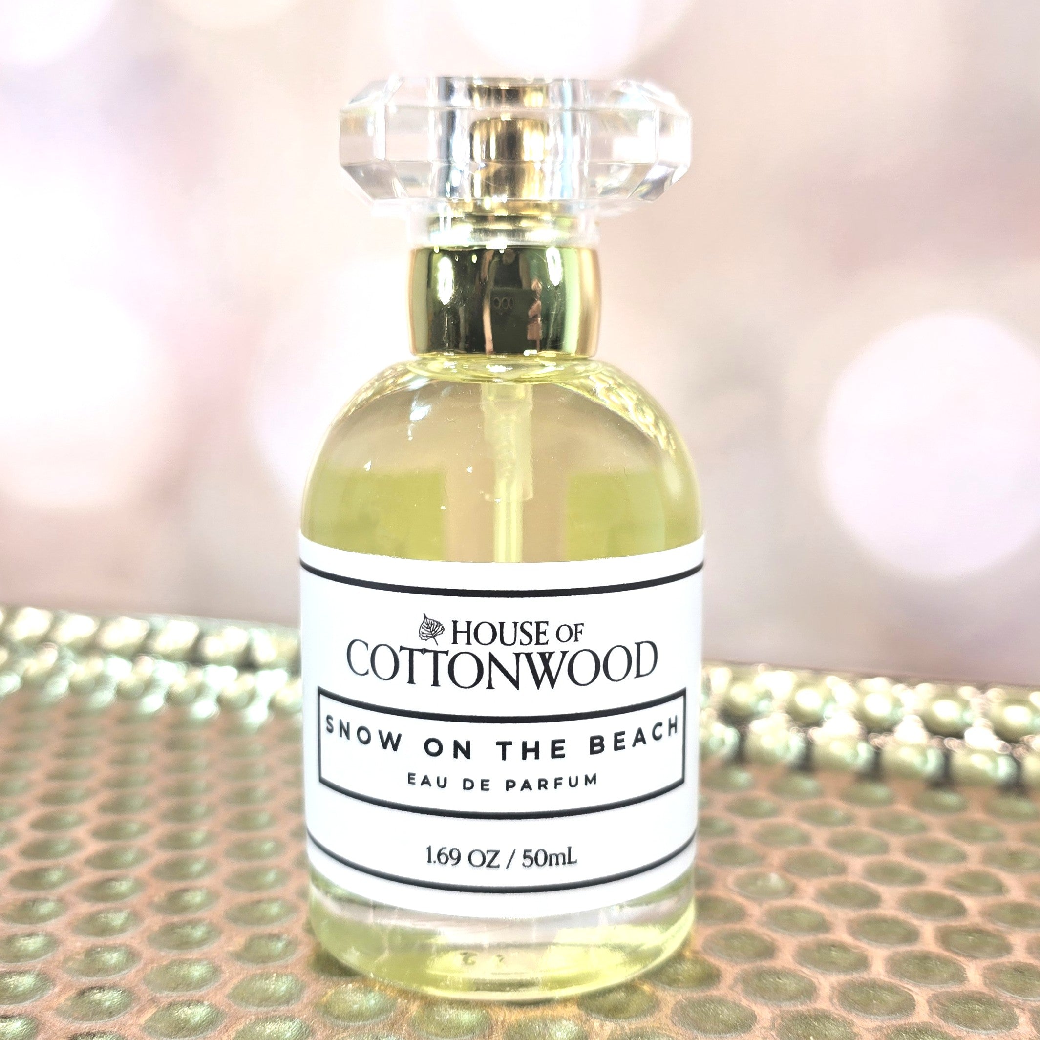 Perfume bottle labeled 'House of Cottonwood Snow on the Beach' on a reflective surface.