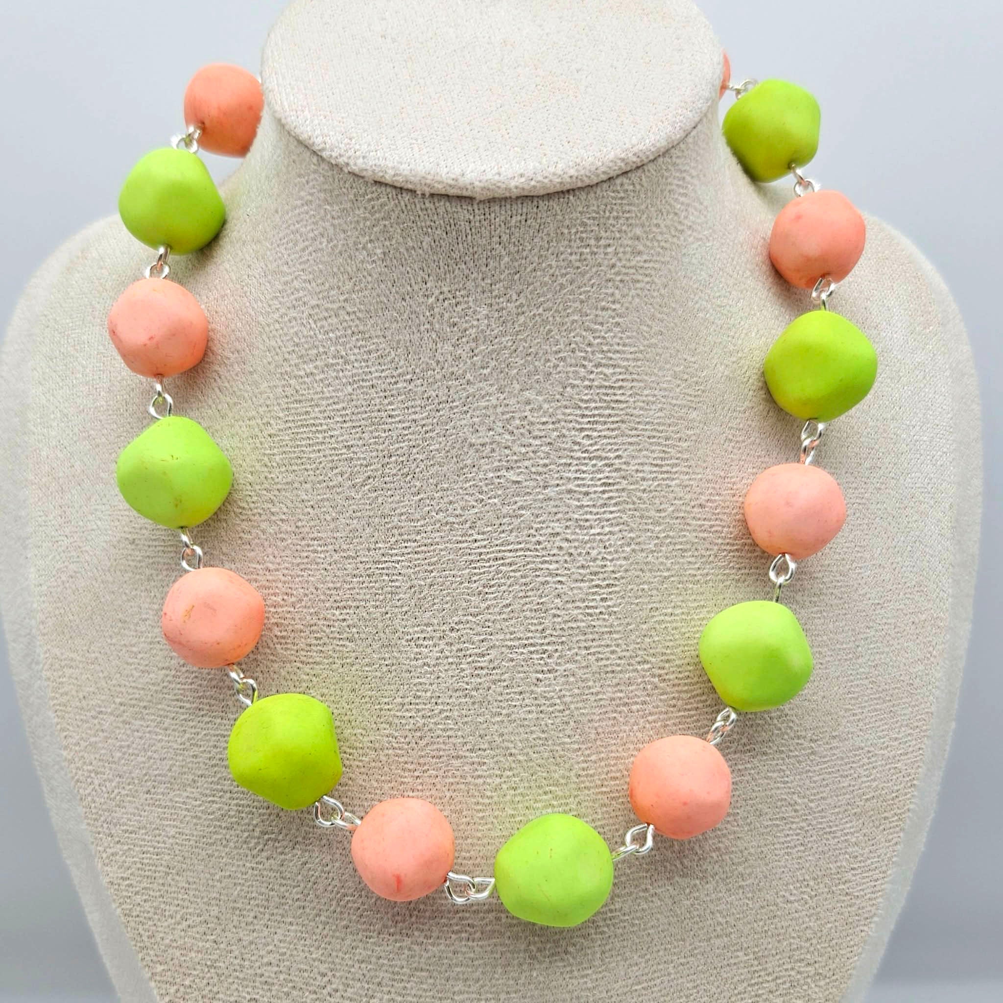 Peach and lime green beaded necklace on a cream colored bust.