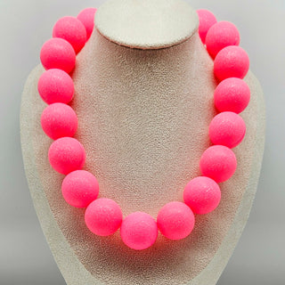 Necklace with pink beads on a beige display stand against a light gray background