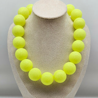 Neon yellow bead necklace on a beige jewelry display
